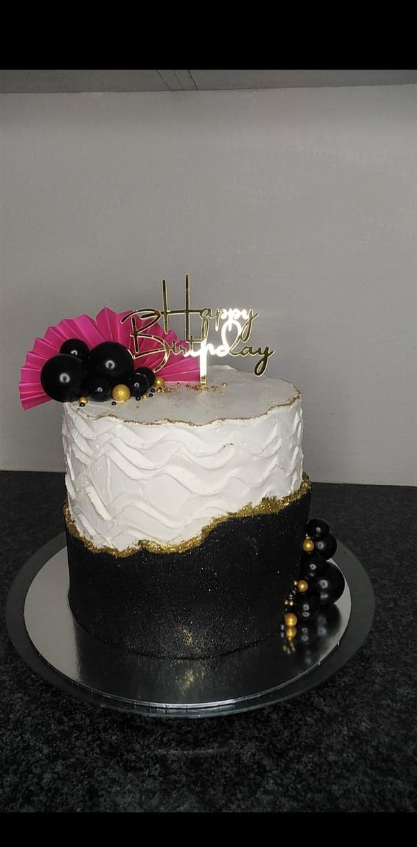 Black and white birthday cake with gold leaf and a pink fan topper