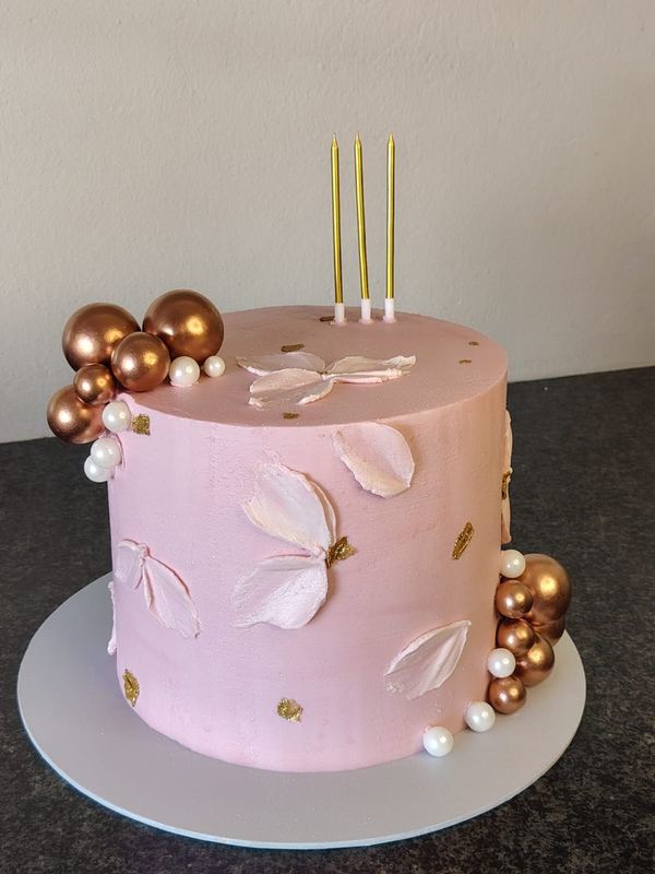 Blush pink birthday cake with fondant petals, bronze spheres and gold candles