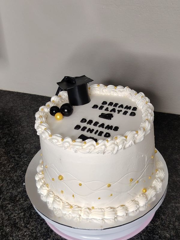 White graduation cake reading Dreams Believed Dreams Achieved with a mortarboard topper