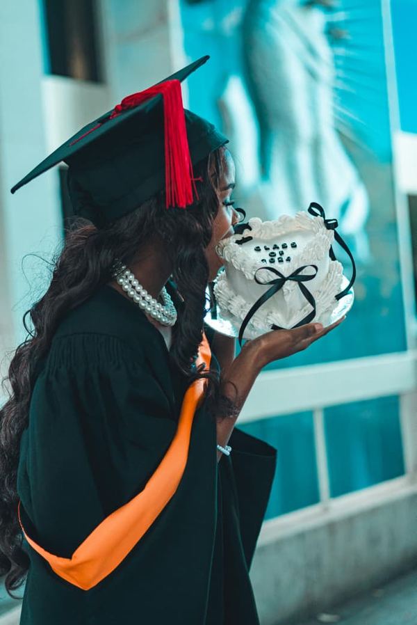Graduate in cap and gown holding a heart graduation cake
