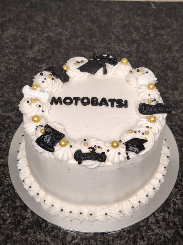 White personalised graduation cake with black mortarboard and scroll decorations