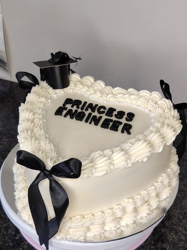 White heart graduation cake reading Princess Engineer with black bows and a mortarboard topper