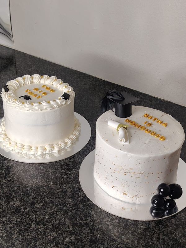 Two white graduation cakes with gold and black details