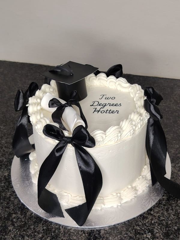 White heart graduation cake reading Two Degrees Hotter with black bows and a mortarboard