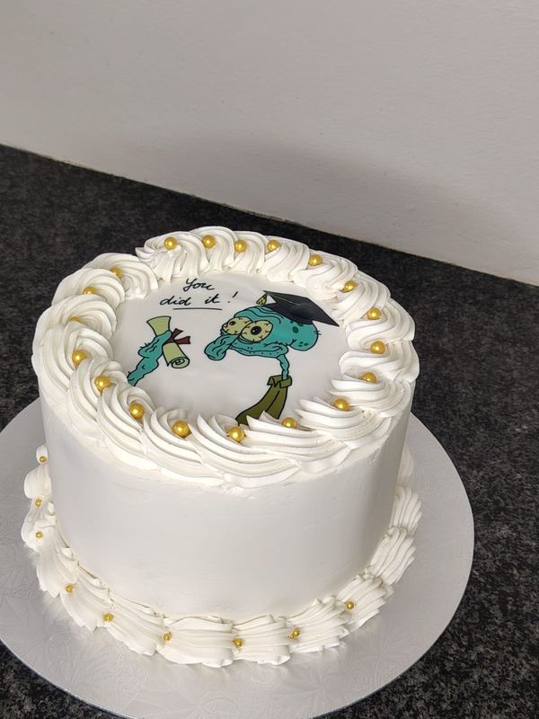 White graduation cake with a printed cartoon graduate and gold pearls