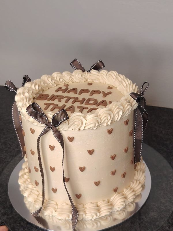 Cream birthday cake with brown hearts and ribbon bows